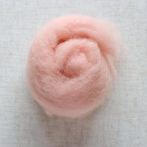 May include: A close-up of a ball of light pink wool roving. The wool is soft and fluffy, and it is perfect for felting or spinning.