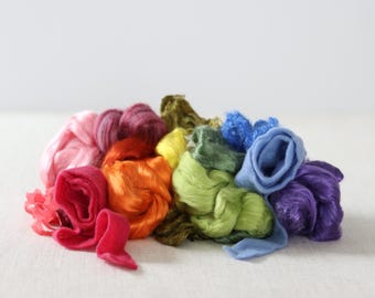 Könnte beinhalten: Eine Sammlung bunter Seidenfasern in den Farben Rosa, Rot, Orange, Gelb, Grün, Blau und Lila. Die Fasern sind in einem lockeren Haufen angeordnet und erzeugen einen Regenbogeneffekt.