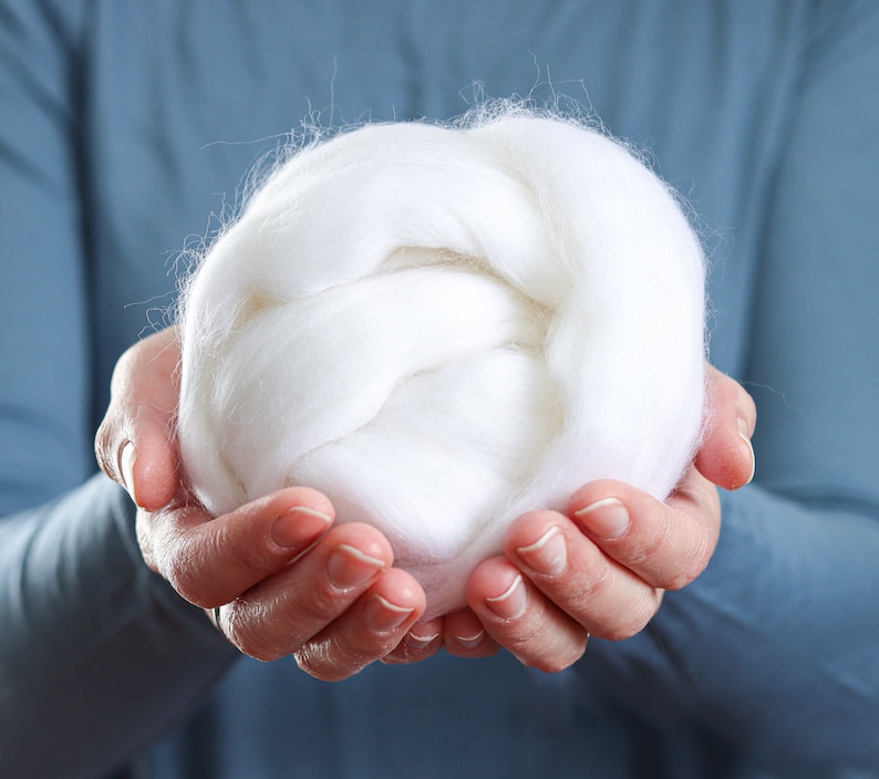 May include: A person's hands holding a large ball of white wool fiber.