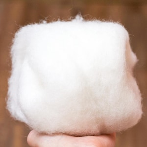 Puede incluir: Una gran bola de fibra de lana blanca y esponjosa. La lana es suave y parece ser muy fina.