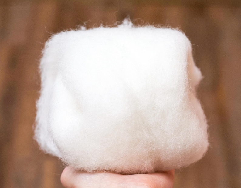 May include: A large, fluffy ball of white wool fiber. The wool is soft and appears to be very fine.
