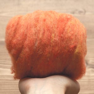 May include: A close-up of a bright orange and yellow wool roving. The roving is soft and fluffy, and it is perfect for felting or spinning.