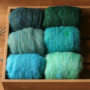 May include: Six balls of wool yarn in a wooden box. The yarn is shades of green and blue, with a gradient effect from dark green to light blue.