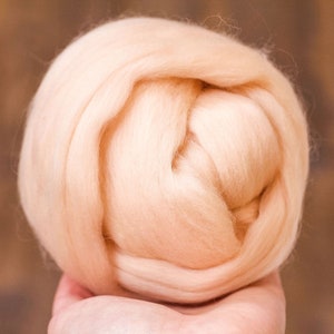 May include: A close-up of a ball of light peach-colored wool fiber. The wool is soft and fluffy, and it is perfect for felting or spinning.
