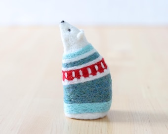 May include: A white felt polar bear wearing a blue, white, and red striped sweater. The sweater has a red band with white dots.