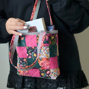 May include: A patchwork tote bag with a floral and geometric pattern. The bag features a mix of pink, green, and floral fabrics, with striped straps. The bag is filled with books.