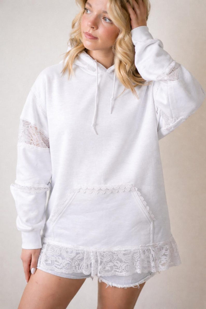 May include: White hoodie with lace accents on the sleeves, pocket, and hem. The hoodie has a drawstring and a front pocket. The lace detailing adds a delicate touch to the casual design. The garment is made of a soft, comfortable material.