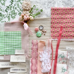 May include: A collage of fabrics and embellishments in shades of pink, green, and cream. Includes floral prints, ribbons, lace, and small decorative items like a clock and a bow. Text snippets read "Bloom", "Wildflower", and "Threads Tell Stories".