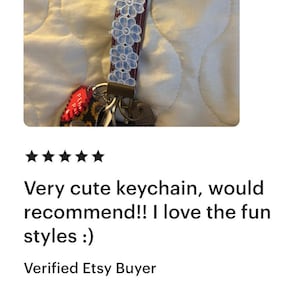 May include: A keychain with a burgundy strap adorned with light blue floral accents. The keychain is attached to a set of keys. The image also includes the text "Very cute keychain, would recommend!! I love the fun styles :)"
