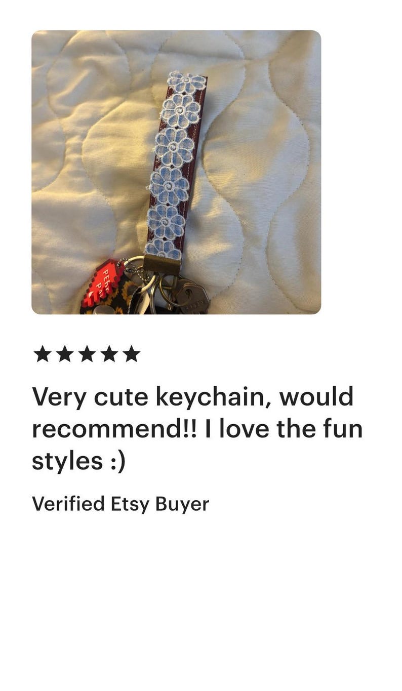 May include: A keychain with a burgundy strap adorned with light blue floral accents. The keychain is attached to a set of keys. The image also includes the text "Very cute keychain, would recommend!! I love the fun styles :)"