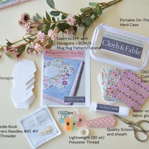 May include: A craft kit with various sewing supplies, including fabric squares, hexagon papers, a needle book, scissors, and a glue stick. The kit also includes a pattern and tutorial for a hexagon flower mug rug. The kit includes a portable hard case.