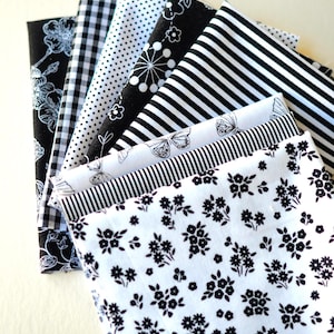 May include: A collection of black and white patterned fabrics, including floral, polka dot, striped, and gingham designs. The fabrics are arranged in a fan shape, showcasing the variety of patterns and textures.