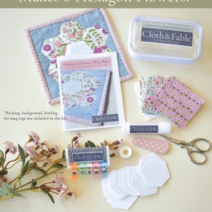 May include: A craft kit for making hexagon flower mug rugs. The kit includes fabric, paper pieces, clips, scissors, and a glue stick. The text on the packaging reads "Makes 6 Hexagon Flowers!" and "Cloth & Fable".