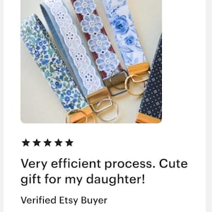 May include: Close-up of several key fobs with various floral and lace patterns in shades of blue and white. Each fob has a gold-colored metal clasp and ring. The image includes text that reads "Very efficient process. Cute gift for my daughter!"