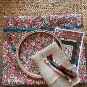 Pode incluir: Uma bolsa de projeto de tecido floral com z&iacute;per turquesa, um bastidor de bordado de madeira, tecido de linho e linha de bordar. Um padr&atilde;o Plum Street Samplers tamb&eacute;m est&aacute; inclu&iacute;do. A bolsa apresenta um padr&atilde;o floral rosa e vermelho.