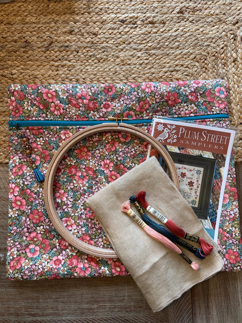 Pode incluir: Uma bolsa de projeto de tecido floral com z&iacute;per turquesa, um bastidor de bordado de madeira, tecido de linho e linha de bordar. Um padr&atilde;o Plum Street Samplers tamb&eacute;m est&aacute; inclu&iacute;do. A bolsa apresenta um padr&atilde;o floral rosa e vermelho.