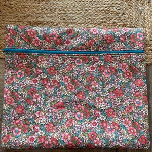Pode incluir: Uma bolsa retangular com estampa floral e z&iacute;per turquesa. O tecido apresenta um padr&atilde;o denso de flores rosa, vermelhas e brancas com folhas verdes sobre um fundo escuro. A bolsa &eacute; provavelmente usada para armazenamento.
