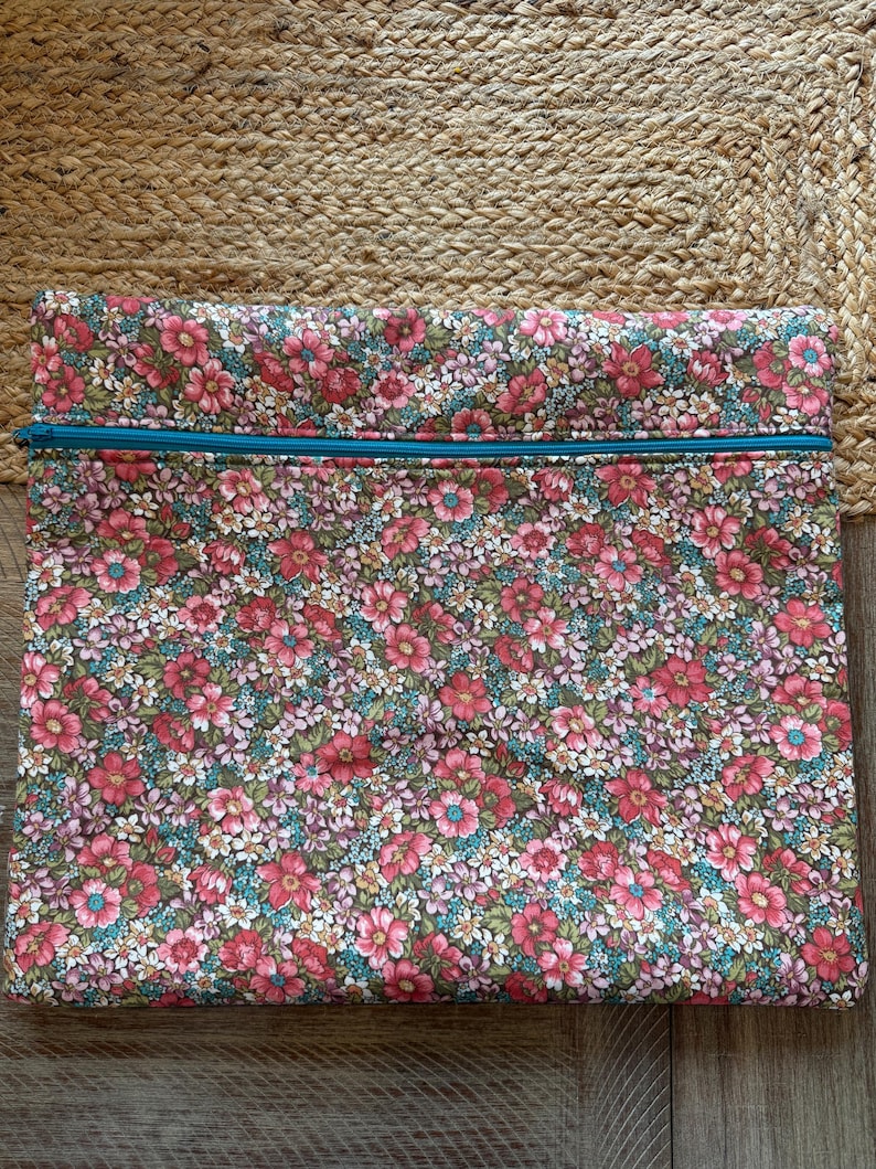 Pode incluir: Uma bolsa retangular com estampa floral e z&iacute;per turquesa. O tecido apresenta um padr&atilde;o denso de flores rosa, vermelhas e brancas com folhas verdes sobre um fundo escuro. A bolsa &eacute; provavelmente usada para armazenamento.