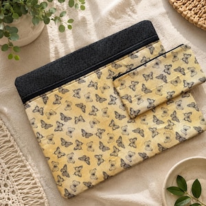 May include: Two fabric pouches, one large and one small. Both have a yellow background with black butterfly patterns. The top of the larger pouch is black. The pouches are displayed on a cream-coloured surface.