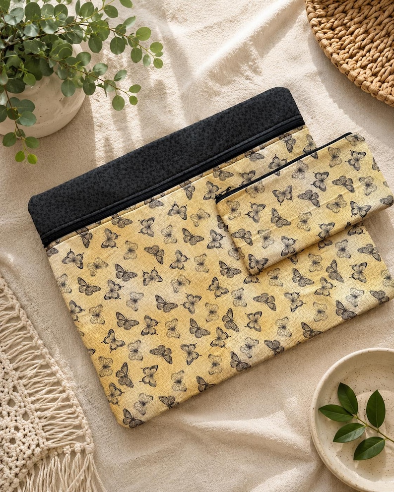May include: Two fabric pouches, one large and one small. Both have a yellow background with black butterfly patterns. The top of the larger pouch is black. The pouches are displayed on a cream-coloured surface.