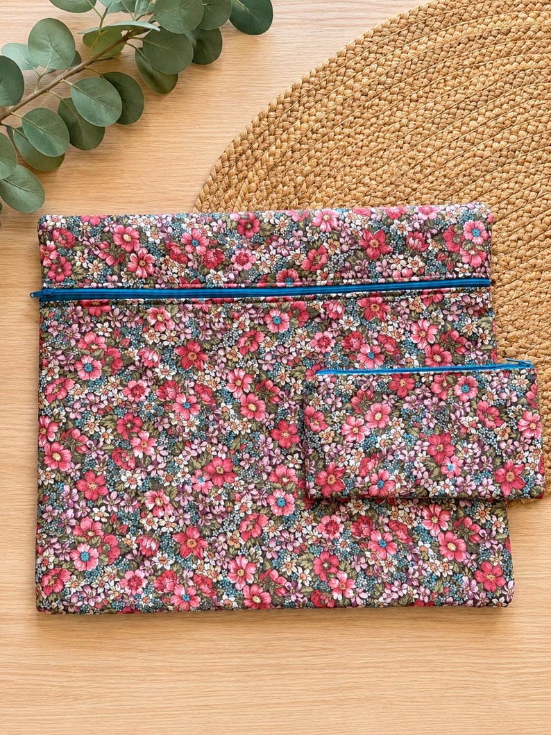 Pode incluir: Um conjunto de bolsas de tecido com padr&atilde;o floral, composto por uma bolsa grande com z&iacute;per e outra menor. O tecido apresenta um padr&atilde;o de flores rosa e vermelhas com detalhes verdes e azuis. Os z&iacute;peres s&atilde;o de um azul brilhante.