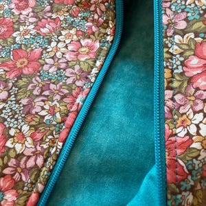 Pode incluir: Close-up de um tecido com padr&atilde;o floral com um fecho de correr turquesa. O tecido apresenta um fundo castanho com flores rosa, vermelhas, brancas e azuis. O forro interior &eacute; de cor turquesa lisa.