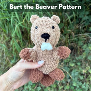 May include: A handmade, plush beaver toy in shades of brown, with a black nose and small black eyes. The beaver has a white tuft of fur under its nose and brown paws and feet. The text "Bert the Beaver Pattern" is at the top.