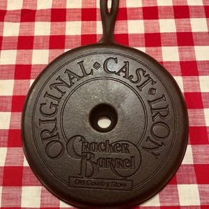 May include: A dark brown cast iron lid with a handle. The lid is round with the words "ORIGINAL CAST IRON" around the edge. The center has the "Cracker Barrel Old Country Store" logo.
