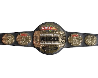 Puede incluir: Un cinturón de campeonato de lucha libre dorado y negro. El cinturón presenta el texto "NWA" y "WILDSIDE" en letras doradas. El cinturón está hecho de cuero negro y tiene detalles dorados.
