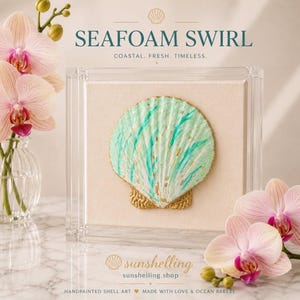 May include: A square clear acrylic frame containing a textured seashell painted in seafoam green with gold leaf accents, mounted on a cream-coloured fabric background. The text SEAFOAM SWIRL, COASTAL. FRESH. TIMELESS. and sunshelling.shop are visible.