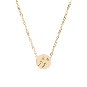May include: A gold-colored necklace with a delicate chain and a circular pendant. The pendant features a detailed engraving of two sets of animal footprints. The necklace is displayed against a white background.