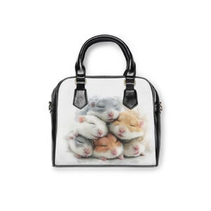 May include: A white handbag with a black handle and trim. The bag features a watercolor image of a pile of sleeping hamsters in shades of gray, white, and tan. The bag has a top handle and a shoulder strap.