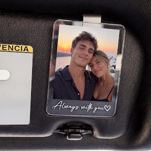 Op de afbeelding: Een rechthoekige, doorzichtige acryl zonneklepclip met een afgedrukte foto van een koppel bij zonsondergang. Het onderste gedeelte van het acrylframe bevat de witte cursieve tekst Always with you, gevolgd door een klein hartje.