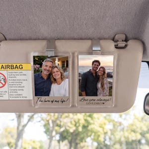 May include: Two rectangular clear acrylic photo frames clipped to a car sun visor. The left frame shows a couple with the text The love of my life! The right frame shows a couple by the ocean with the text Love you always! LOVE.EMILY.