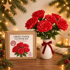 Puede incluir: Un kit de flores de papel crepé en una caja de cartón marrón etiquetada Crepe Paper Flower Kit Eternal Roses con un icono de tutorial en video y cinco rosas rojas más hojas. Junto a ella, un jarrón de cerámica blanca contiene cinco rosas.