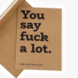 Könnte beinhalten: Eine Grußkarte aus braunem Kraftpapier mit passendem Umschlag. Die Karte zeigt einen fetten schwarzen Text mit der Aufschrift: "You say fuck a lot. I like that about you." Das Design ist schlicht, wobei der Text auf der Vorderseite zentriert ist.