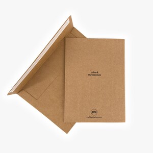 May include: A brown greeting card and envelope set. The card reads "cake & threesomes" in a simple black font. The envelope is open, revealing the adhesive strip. The Etsy shop's logo and website are printed on the card.