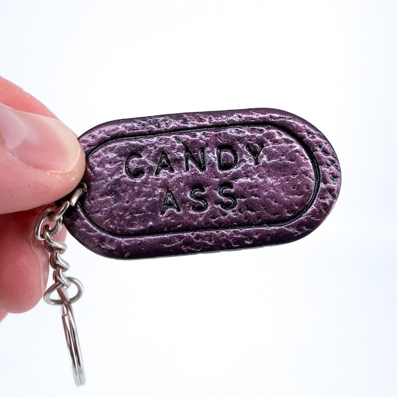 A hand-sculpted polymer clay keychain spelling out 'Candy Ass' — small, genuinely handmade, and delivers a perfectly rude punchline every time you grab your keys.