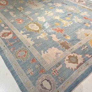 May include: A large, rectangular rug with a light blue background and intricate floral patterns in shades of cream, orange, yellow, and purple. The rug features a detailed border and the text "RUG CHIC".
