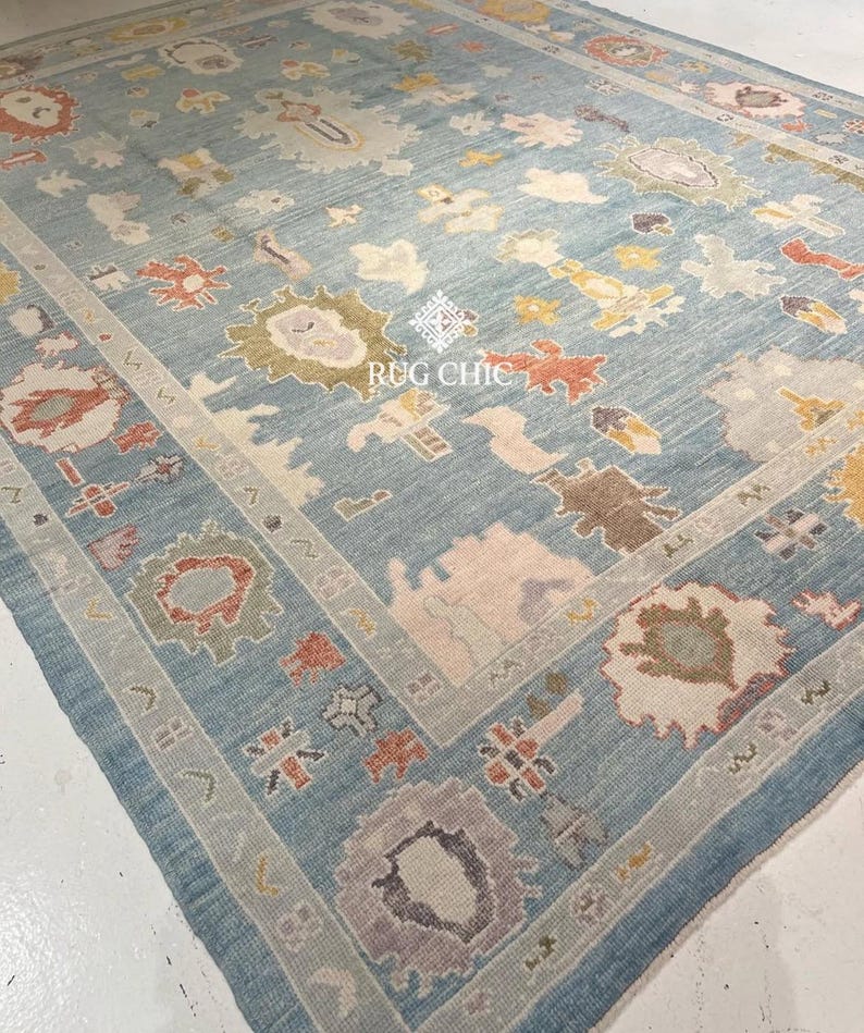 May include: A large, rectangular rug with a light blue background and intricate floral patterns in shades of cream, orange, yellow, and purple. The rug features a detailed border and the text "RUG CHIC".