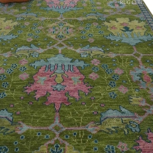 May include: A green area rug with a detailed floral pattern in pink and blue. The rug has a distressed look and a fringe border. The words "RUG CHIC" are visible in the upper right corner. The rug is a decorative home decor item.