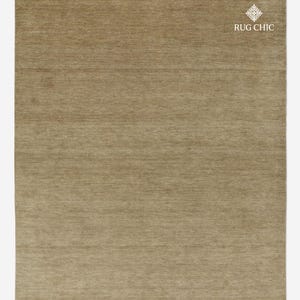 May include: A rectangular, neutral-toned rug with a textured surface. The rug is a solid color, with a subtle sheen, and the text "RUG CHIC" is visible in the upper right corner.