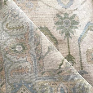 May include: A rolled-up area rug with a detailed floral pattern. The rug features a cream-colored background with accents of blue, green, and tan. The design includes stylized floral and geometric shapes, creating a vintage aesthetic.