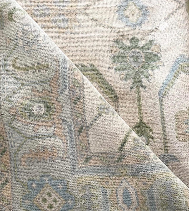 May include: A rolled-up area rug with a detailed floral pattern. The rug features a cream-colored background with accents of blue, green, and tan. The design includes stylized floral and geometric shapes, creating a vintage aesthetic.