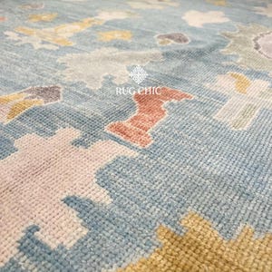 May include: Close-up of a blue rug with a geometric pattern. The rug features a mix of colors, including light blue, pink, yellow, and orange. The text "RUG CHIC" is visible on the rug.