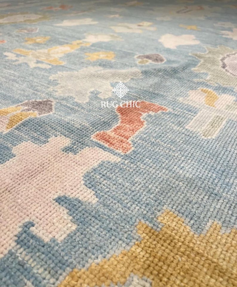 May include: Close-up of a blue rug with a geometric pattern. The rug features a mix of colors, including light blue, pink, yellow, and orange. The text "RUG CHIC" is visible on the rug.