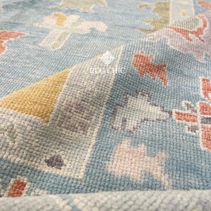 May include: Close-up of a light blue rug with a detailed pattern. The rug features a mix of colors, including peach, yellow, and gray, creating a textured appearance. The text "RUG CHIC" is visible on the rug.