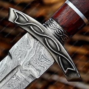 May include: Close-up of a dagger with a patterned blade and a decorative metal guard. The handle is dark wood with a silver band. The blade has a unique, swirling pattern. The dagger is a handcrafted item.