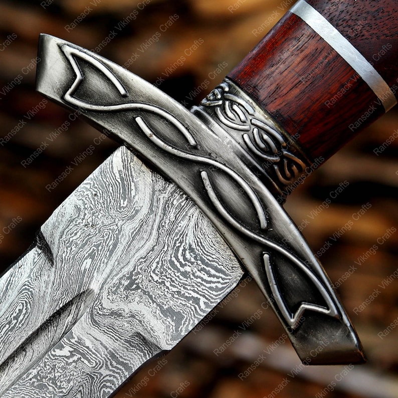 May include: Close-up of a dagger with a patterned blade and a decorative metal guard. The handle is dark wood with a silver band. The blade has a unique, swirling pattern. The dagger is a handcrafted item.