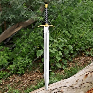 May include: A long, silver sword with a gold crossguard and pommel. The handle is black with a textured design. The sword is displayed against a backdrop of green foliage and a wooden log.